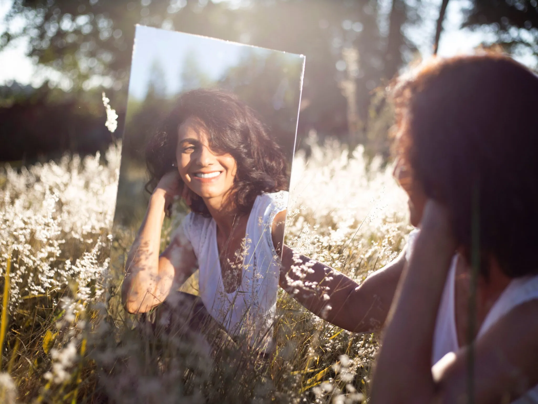 Femme souriante dans un champ, reflétée dans un miroir : se reconnecter à la nature
